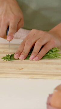 Vertical video: Placing herb bundle, hands chopping chives on wood board with knife, eggs for meal
