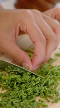 Vertical video: Chopping hands guiding knife on board for prep, sweeping herb pile for garnish