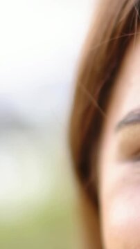 Vertical video: Reaching hand, female tucking hair for camera, holding right eye contact in park