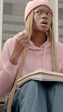 Vertical video: Leaning forward woman in pink hoodie opening notebook, reading on steps, rehearsing