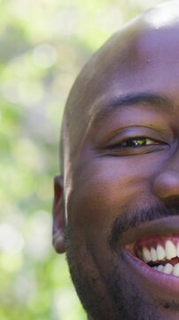 Vertical video: Smiling shaved-head man deepening grin while camera rolling in park, showing warmth
