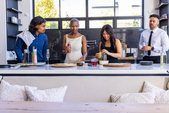 Diverse friends standing at kitchen island, preparing drinks and squeezing citrus with glassware