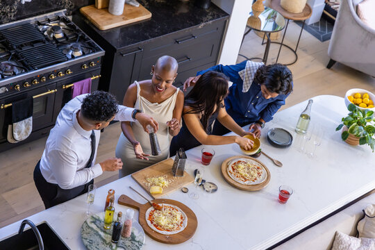 African American friends making pizzas on white marble island using wooden boards, seasoning pepper