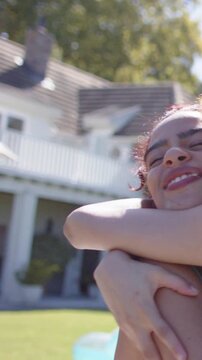 Vertical video: Friend hugging front woman in yard by house after arm raising, playful, swimsuit