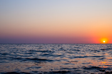 Fototapeta premium A scenic sunset over the sea with gentle waves on a summer evening. coastal nature view, beautiful sea sunset, summer vacation getaway.