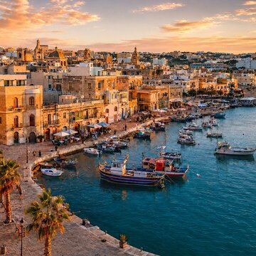 Cidade hist&oacute;rica &agrave; beira-mar com barcos de pesca ao p&ocirc;r do sol.