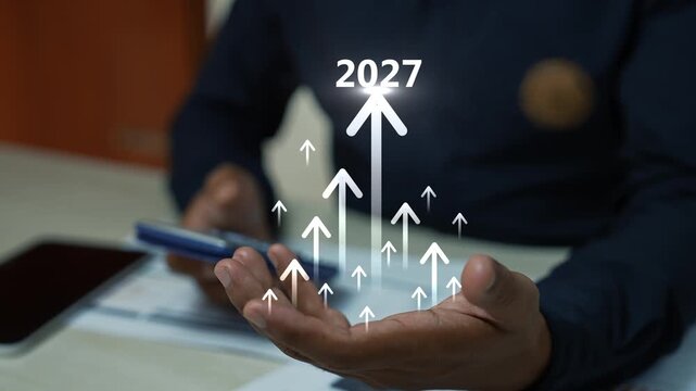 Business person holding a calculator with glowing hologram  2027 upward arrows above an open hand, showing growth success, progress and digital business performance in a modern office