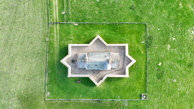A top-down aerial view of Corgarff Castle in Scotland, showing its full star-shaped fortified layout and surrounding Highland terrain from directly above, with winding roads, green moorland, and rugge
