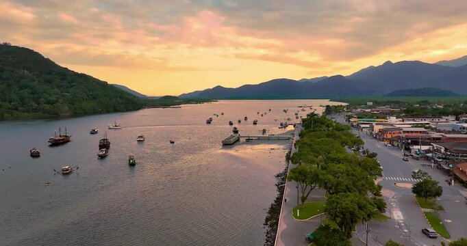 4K drone view of Bertioga fishing harbor at sunset, featuring boats, waterfront, calm waters and coastal landscape on Brazil's coast.