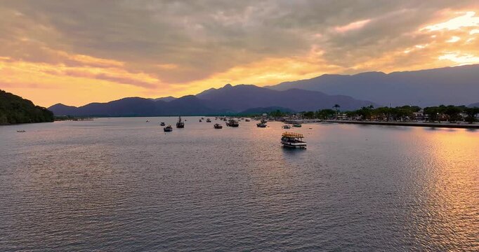 4K drone view of Bertioga fishing harbor at sunset, featuring boats, waterfront, calm waters and coastal landscape on Brazil's coast.