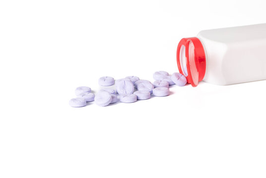Large, round purple chewable tablets spilling out of a white bottle with red lid onto a white background.