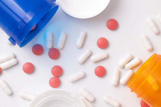 White capsules and pink pills spilled out of orange and blue bottles, scattered over a white background