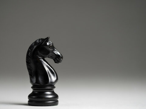 Black knight chess piece standing on surface isolated on gray background.