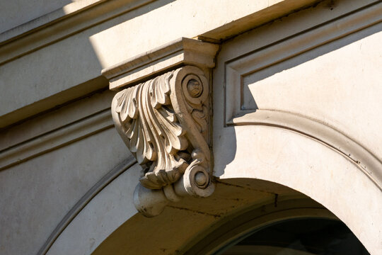 Ornate classic stone corbel supporting a historic building arch with sharp sunlight shadows.