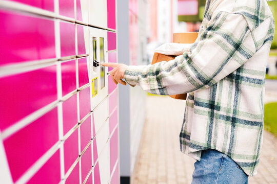 Man holding packages using an automated pink parcel locker terminal. Contactless delivery service, e-commerce online shopping, and modern pickup logistics technology.