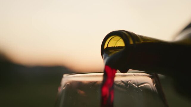 Experience the elegance of red wine flowing into a glass, capturing the beauty of an evening at a peaceful winery bathed in soft sunset light