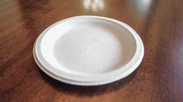 POV view of a person reaching for a glazed donut with a bite taken out of it on a white paper plate