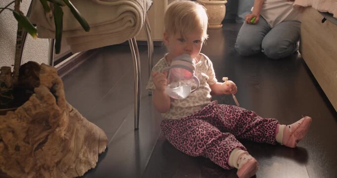 Toddler sitting on the floor and drinking water during everyday life at home. Independent drinking skill and early childhood development