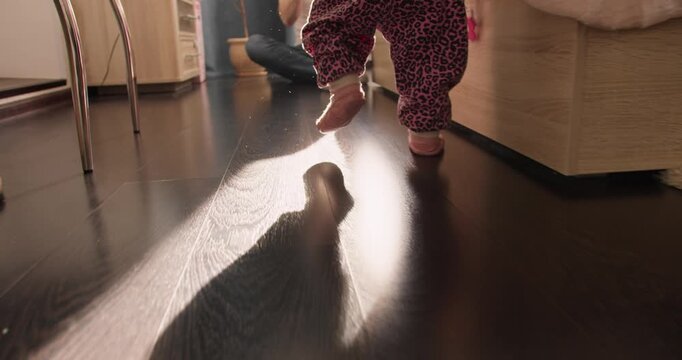 Toddler taking first steps with father nearby. Home scene about parenting, safety and child development