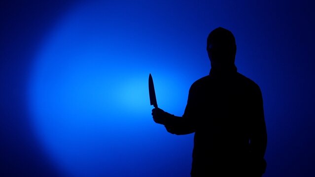 Silhouette of a mysterious person holding a large kitchen knife, creating a chilling atmosphere of fear, crime, and danger against a stark blue backdrop