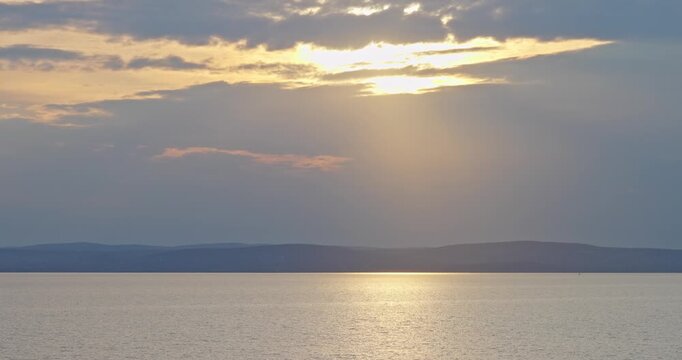 Sun setting over calm lake water and distant mountains