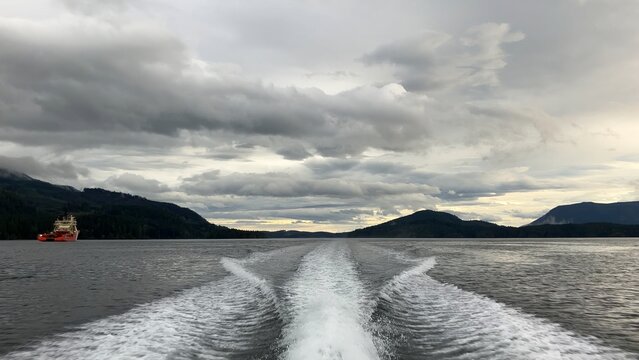 Vessel leaving wake on calm water past coastline