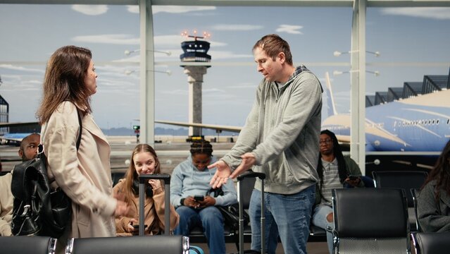 Scolding man, bumping trolley and upset woman in airport hurrying to catch plane, Yelling, bashing luggage and angry tourist with traveler in busy departure terminal, camera A with hectic and crowd.