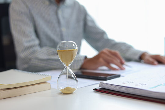 Businessman at a desk with an hourglass in the foreground, representing a time management concept.