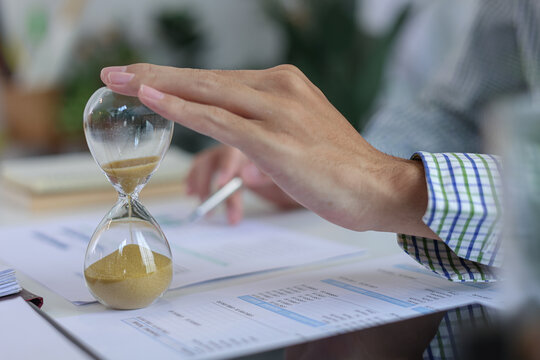 Close up of hand on sandglass for deadline and time management concept.