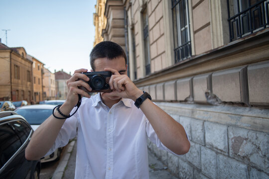 A young man holding a retro camera and taking photos in the city