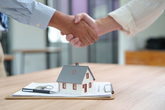 Real Estate Transaction: Key Handshake with House Model and Documents on Table