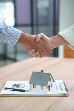 Hands shaking over real estate agreement with house model and keys on table