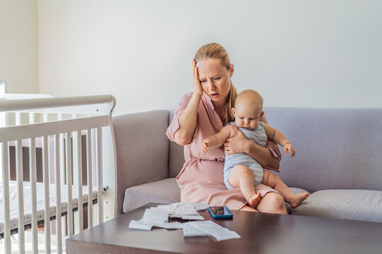 Mother sitting on sofa holding baby while calculating monthly expenses with receipts at home. Stressed mom managing budget and childcare. Financial stress, parenthood and real life concept