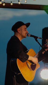 Male guitarist singing on stage at dusk
