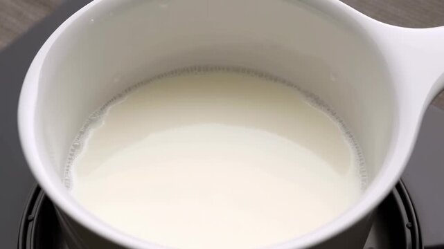 Slow heating process of milk in a white saucepan on stovetop