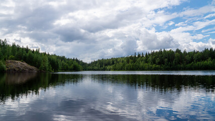 Fototapeta premium Scenic summer view of a calm lake surrounded by a dense green forest under a cloudy sky in Karelia, Russia.