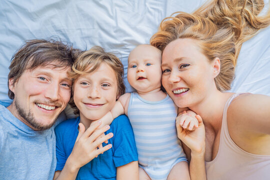 Baby lying on bed with mother, father and older brother at home. Happy family spending time together, bonding and relaxing. Parenthood, sibling connection and warm family life concept