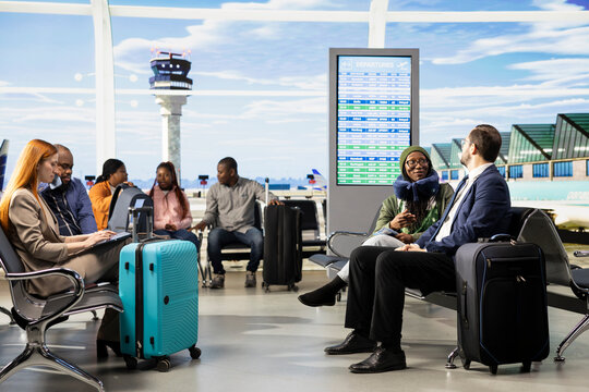 Busy airport terminal with diverse travelers waiting near luggage and backpacks, departures area near gate.