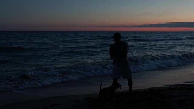 Dark silhouette of a male boxer practicing his punches on the sandy shore with his dog, against a beautiful sunset over the sea, embodying concepts of dedication, training, and freedom