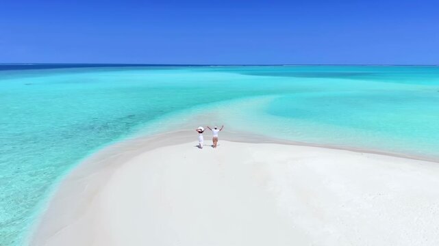 Aerial slow motion view of a happy couple running on a sandbank beach with turquoise, clear water in the Maldives islands