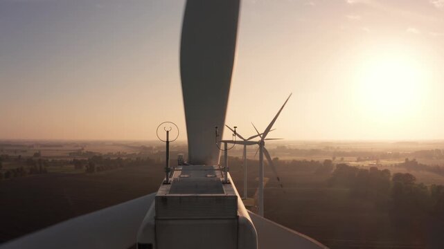 Witness the enchanting dance of wind turbines as they turn in the soft light of dawn. Set against a peaceful countryside, this moment captures nature's harmony and energy