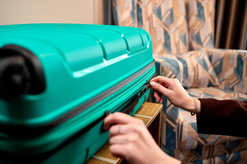 Obraz premium Hands closing a teal hard-shell suitcase on a wooden table