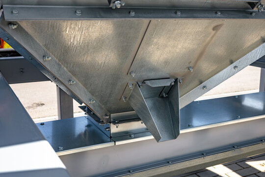 Close-up view of a galvanized metal hopper with an angled chute mounted on a painted steel support frame. The scene shows textured sheet metal, welded seams