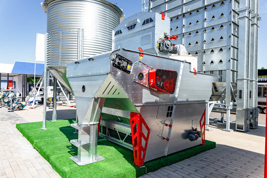 A large stainless steel industrial centrifuge sits on artificial grass outdoors at an exhibition area. The machine features polished metal surfaces