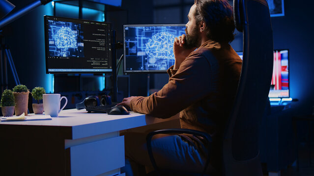 Freelancing programmer writes code on desktop PC to visualize artificial intelligence neural networks, self employed man runs AI script on computer from apartment office, jib down shot.