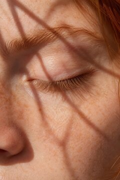 Close up freckled face closed eye red eyelashes. Linear shadows create calm aesthetic atmosphere. Ideal for skincare, beauty, wellness, and natural health marketing materials.