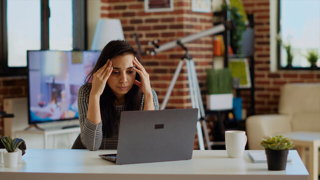 Stressed overworked indian employee struggling to concentrate while working from home, hurting from headache, tired teleworker feeling nausea while working on laptop.