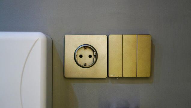 ⁠Minimalist home interior details showcasing elegant golden plastic wall switches and a European-style power outlet