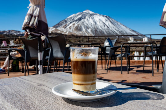 Drinking warm barraquito Canarian speciality coffee made with more layers in high attitude cafe with view on white snow top of Volcano Teide, Tenerife, Spain, winter vacation