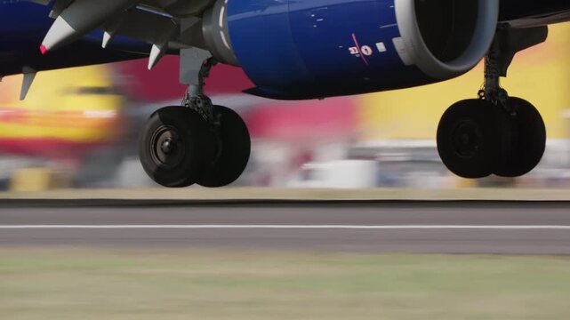 Low angle view of aircraft nose landing gear just above runway during takeoff, twin wheel visible with engine and fuselage above, slow motion, blurred ramp background